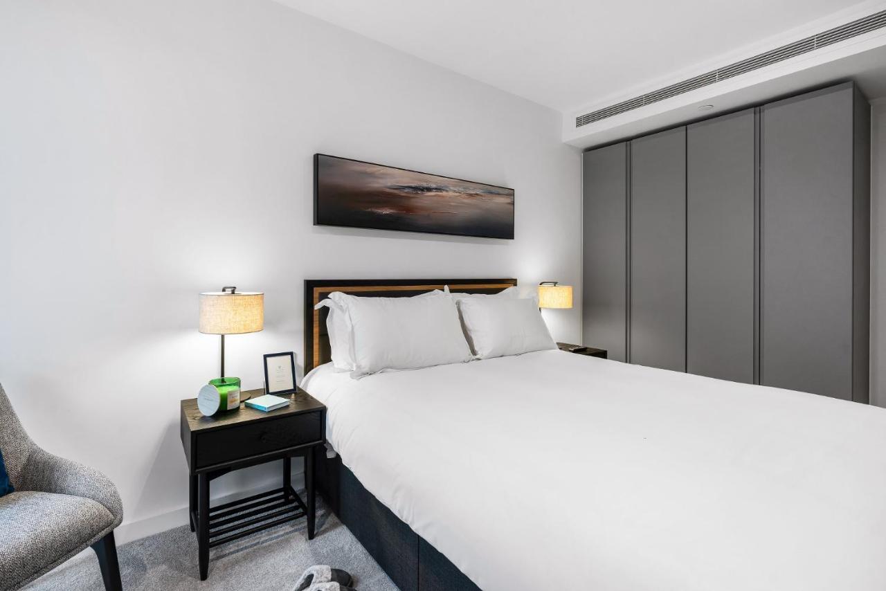 Citysuites 2 Aparthotel Manchester Kültér fotó The photo shows a modern bedroom with a neatly made bed featuring white linens and pillows. Flanking the bed are two bedside tables, each with a lamp providing soft lighting. There is a piece of artwork above the bed, which appears to depict a landsc