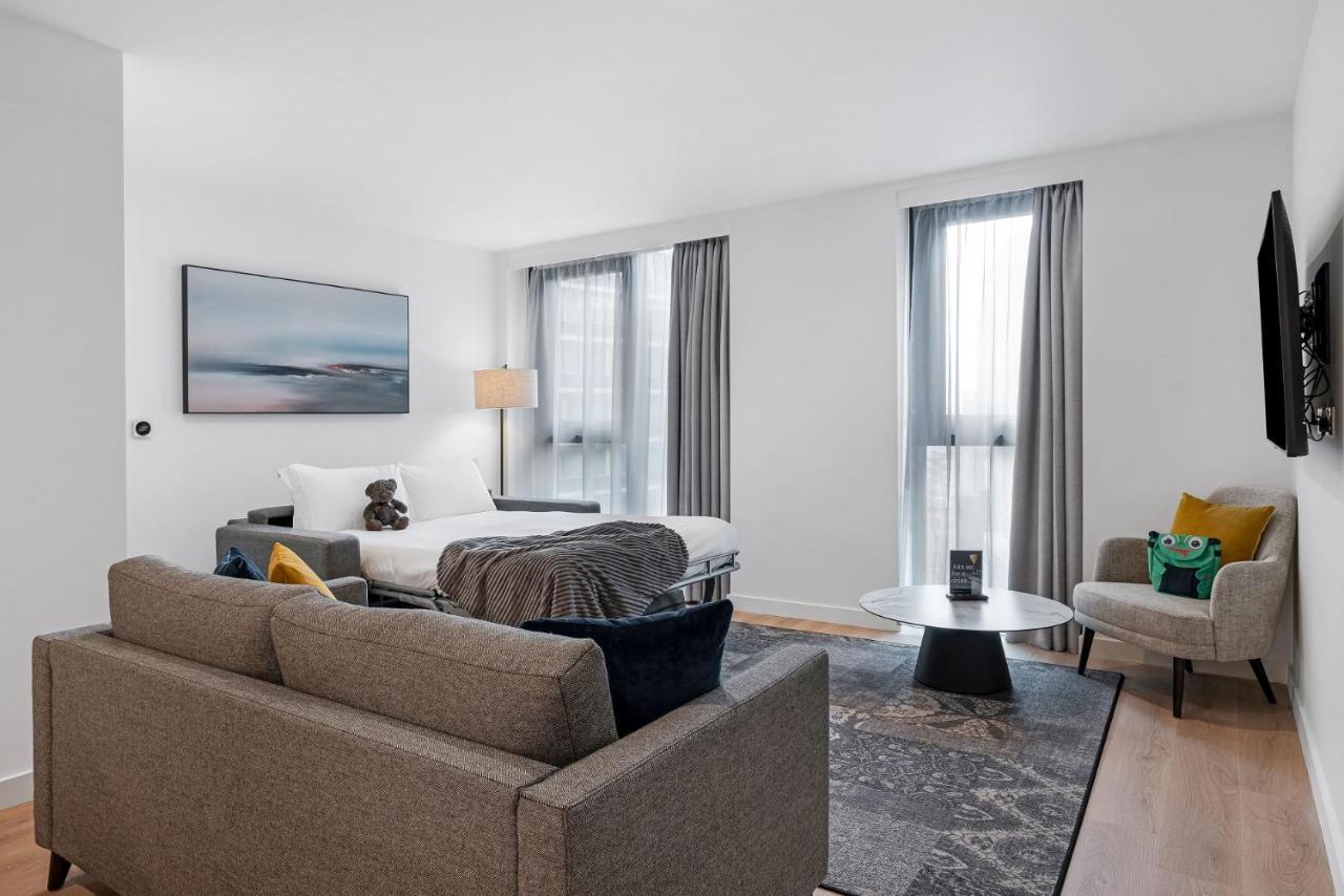 Citysuites 2 Aparthotel Manchester Kültér fotó The photo shows a modern living space that incorporates a cozy and inviting atmosphere. It features a light-colored couch with colorful cushions, positioned in front of a coffee table. There's a comfortable armchair nearby, and a throw blanket is dra