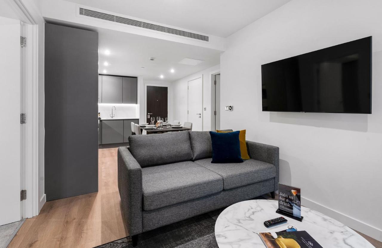 Citysuites 2 Aparthotel Manchester Kültér fotó The photo shows a modern living space that includes a gray sofa with colorful cushions, a round marble coffee table, and a flat-screen TV mounted on the wall. In the background, there is a kitchen area featuring sleek cabinets. The flooring is light 