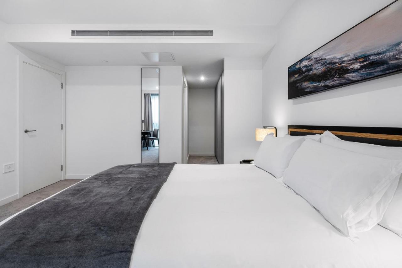 Citysuites 2 Aparthotel Manchester Kültér fotó The photo shows a modern bedroom with a minimalistic design. In the foreground, there is a neatly made bed with white linens and a dark gray throw blanket. To the side, there is a bedside lamp and a piece of abstract artwork on the wall above the bed
