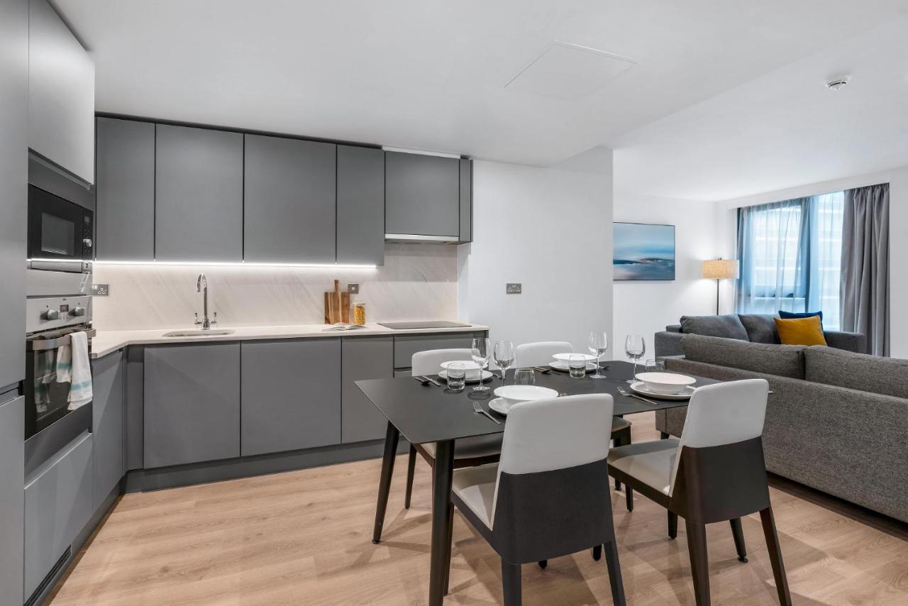 Citysuites 2 Aparthotel Manchester Kültér fotó The photo shows a modern, open-concept kitchen and living area. The kitchen features sleek, gray cabinetry with a countertop, a sink, and built-in appliances. There are cooking utensils displayed on the countertop. Next to the kitchen, there is a din