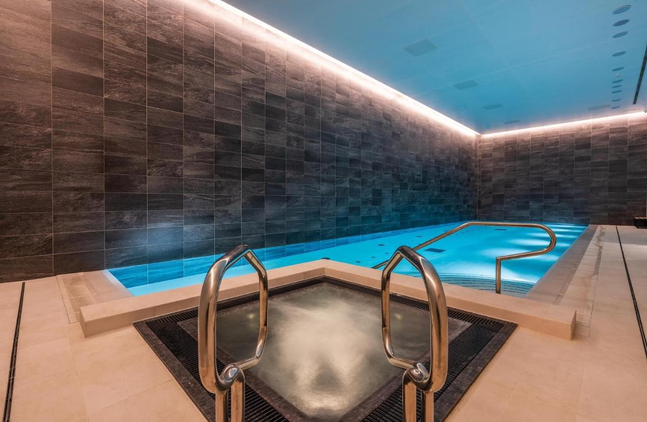 Citysuites 2 Aparthotel Manchester Kültér fotó The photo shows a modern indoor swimming pool area. The pool features a sleek, rectangular design with a beautiful blue water that seems illuminated. Surrounding the pool are dark, textured walls, adding to the elegant atmosphere. There are dual meta