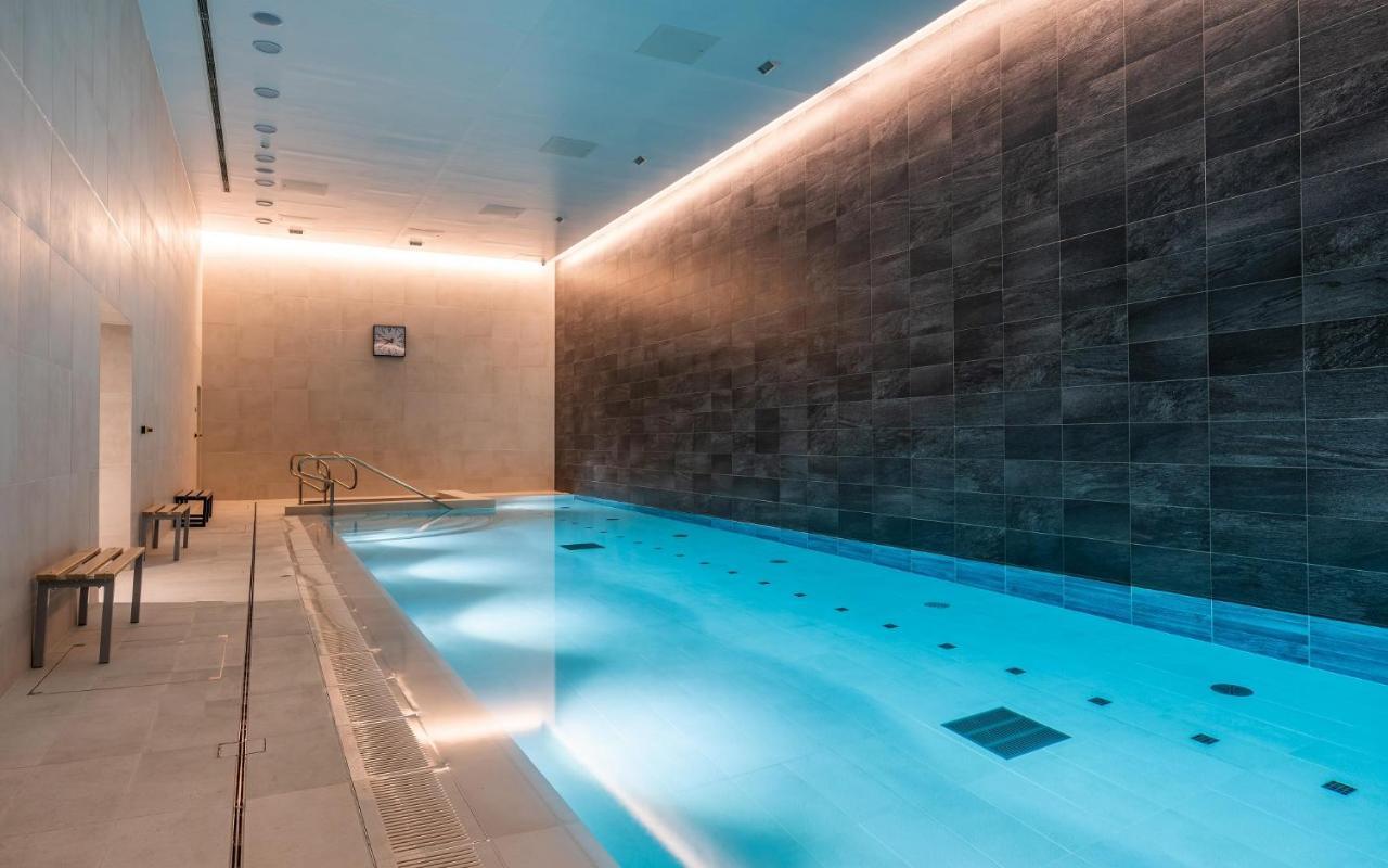 Citysuites 2 Aparthotel Manchester Kültér fotó The photo shows an indoor swimming pool area. The pool is illuminated with a soft blue light, creating a calming atmosphere. The walls are designed with dark tiles, and there is a lighter tiled area surrounding the pool. Ambient lighting is installed