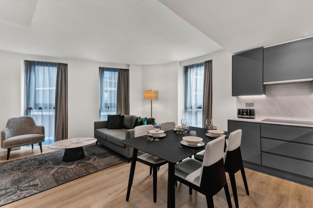 Citysuites 2 Aparthotel Manchester Kültér fotó The photo shows a modern living space that includes a dining area and a seating area. There's a sleek black dining table set with plates and cutlery, accompanied by white and black chairs. To one side, a comfortable gray sofa faces the dining area, c
