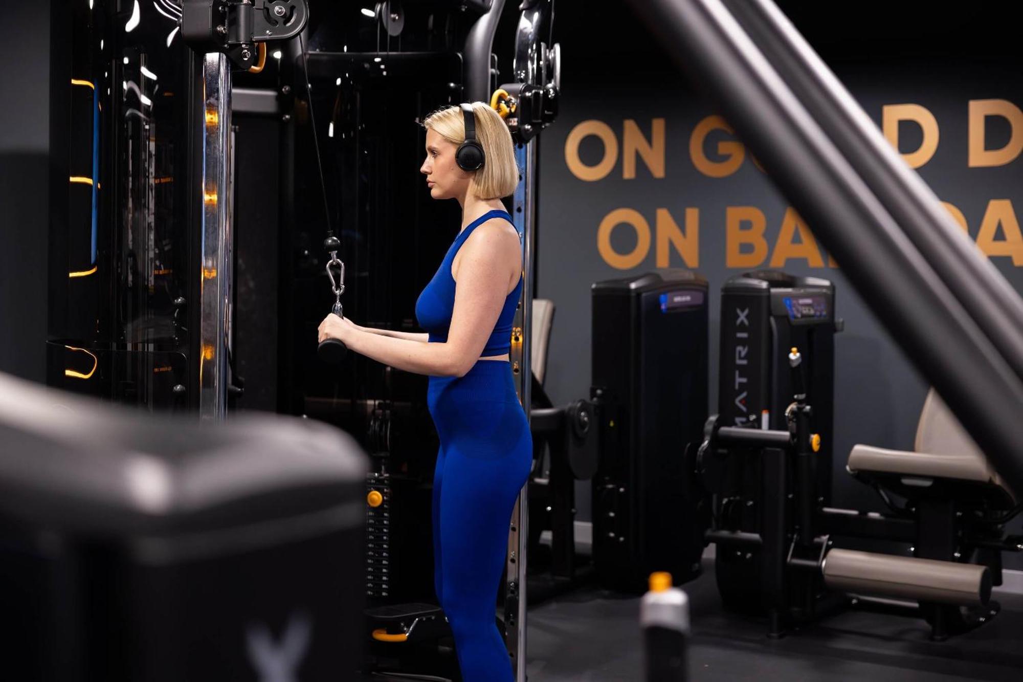 Citysuites 2 Aparthotel Manchester Kültér fotó The photo shows a woman working out in a gym. She is wearing a blue athletic outfit and headphones while using a gym machine. The background features various other gym equipment and a wall with the words "ON GOOD ON BAD" displayed prominently. The se