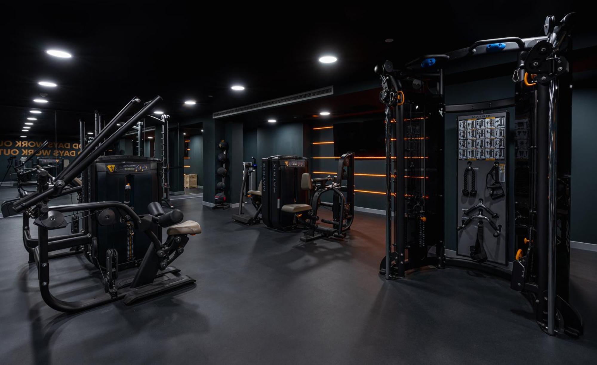 Citysuites 2 Aparthotel Manchester Kültér fotó The photo shows a modern gym or fitness area with various workout machines. The space has a dark color scheme, featuring black walls and flooring. There are multiple pieces of exercise equipment, including stations for strength training, possibly tar