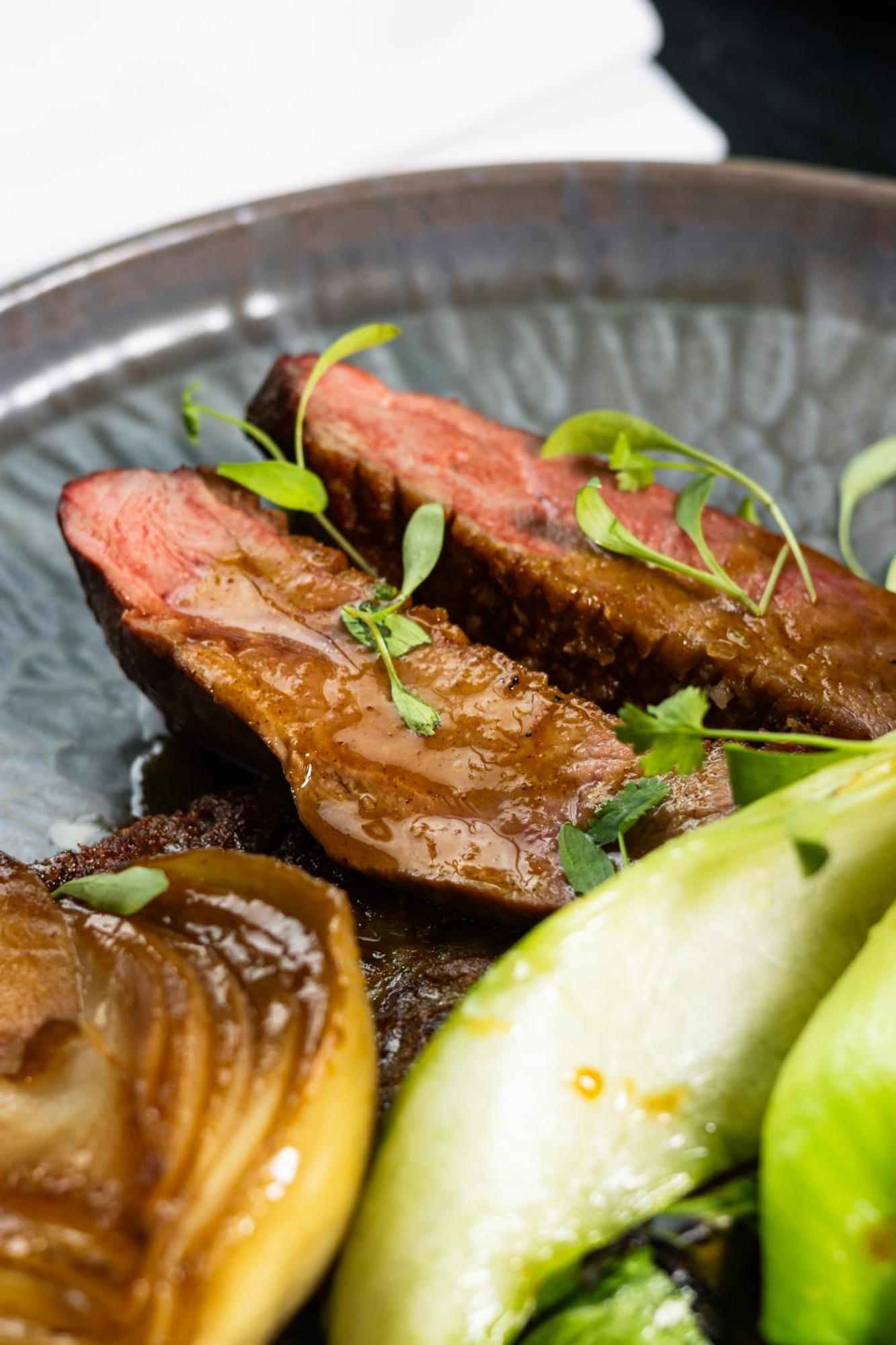Citysuites 2 Aparthotel Manchester Kültér fotó The photo features slices of meat, likely beef, presented on a decorative plate. The meat appears to have a rich brown sauce drizzled over it and is garnished with fresh herbs, adding a pop of green. There are also some slices of a light-colored vege