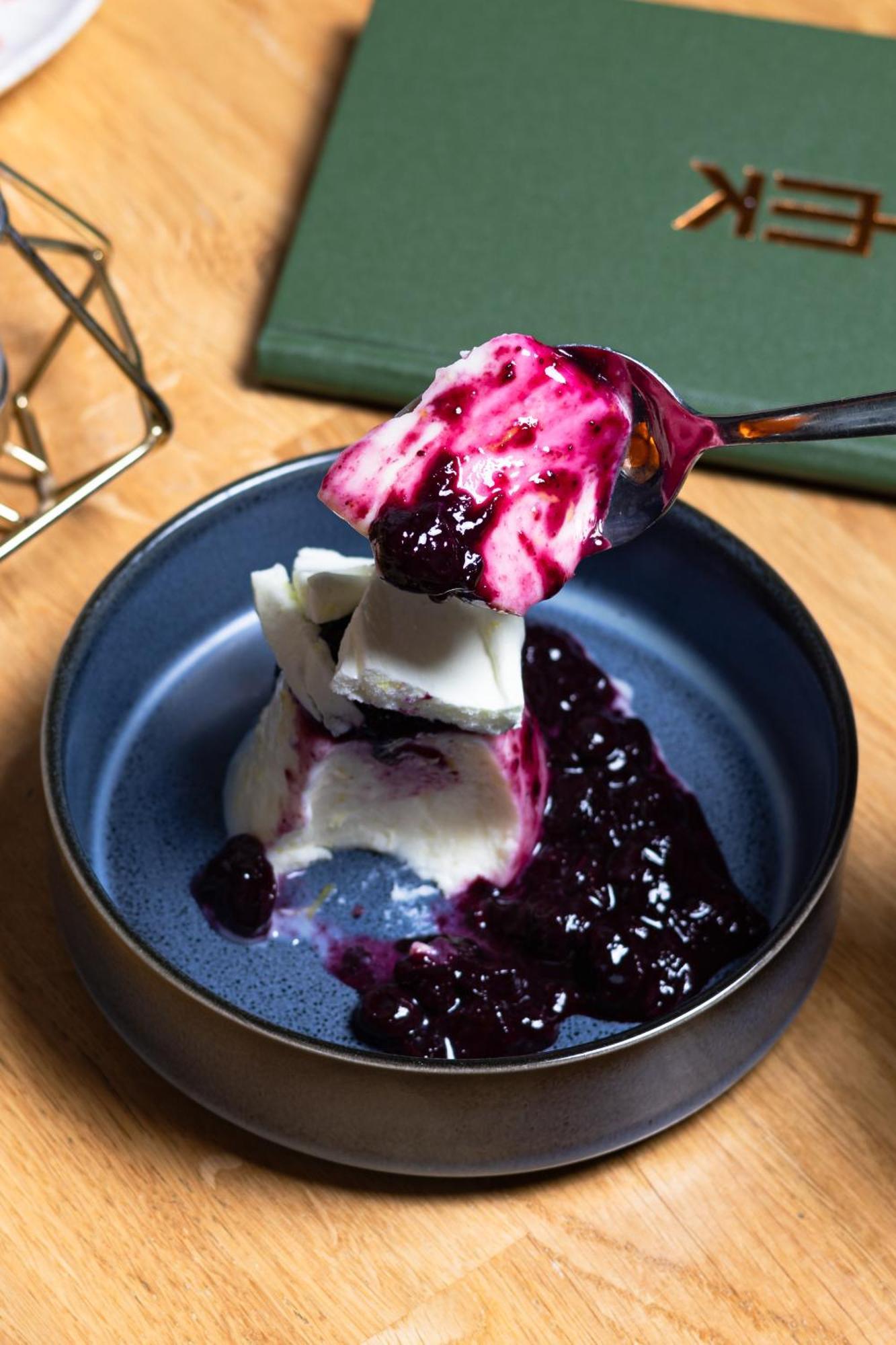 Citysuites 2 Aparthotel Manchester Kültér fotó The photo shows a serving of dessert, likely a type of panna cotta or a creamy custard, partially dished out and accompanied by a rich berry sauce, possibly made from blueberries or blackberries. A spoon with some of the dessert and sauce is hovering